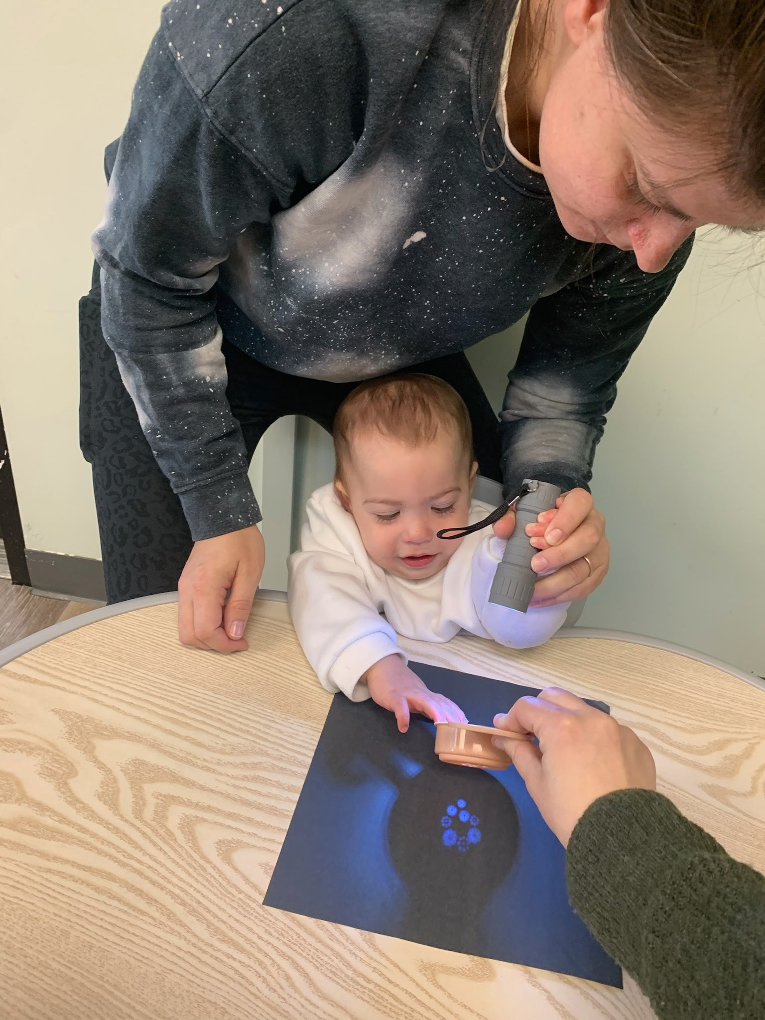 A teacher guiding an infant's hands during an activity at Mighty Sprouts